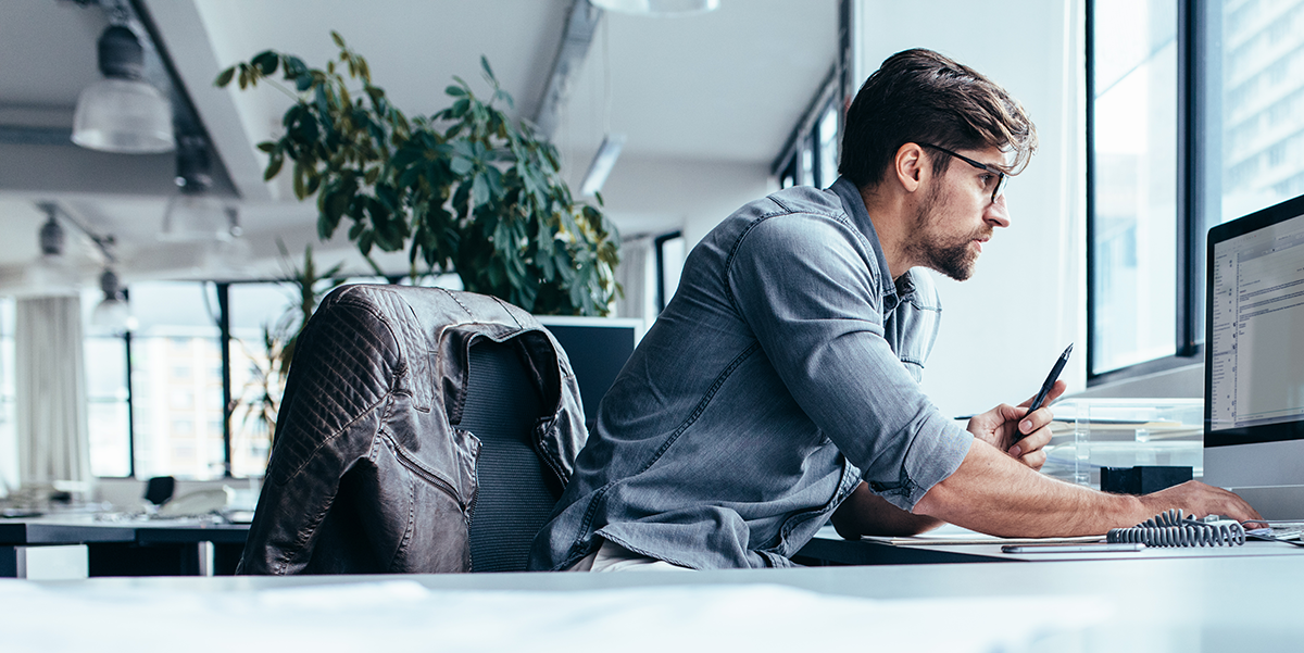 Caucasion man working on his computer at a desk in a corporate office.