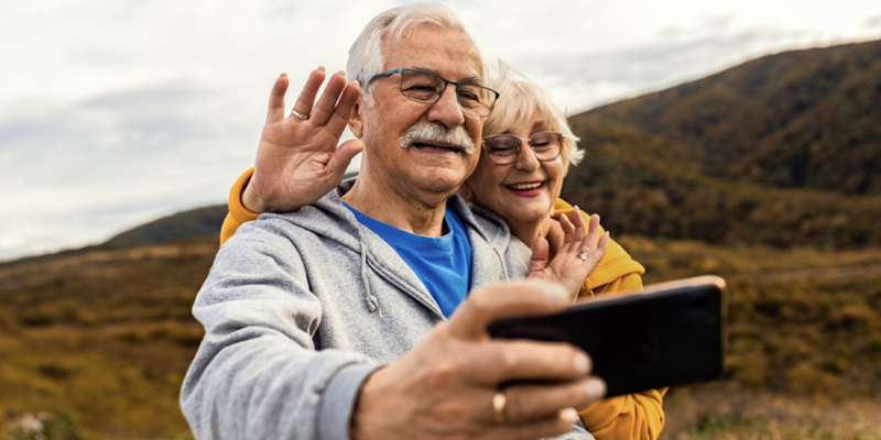 Senior aged couple on a hill side taking a picture on their smart phone
